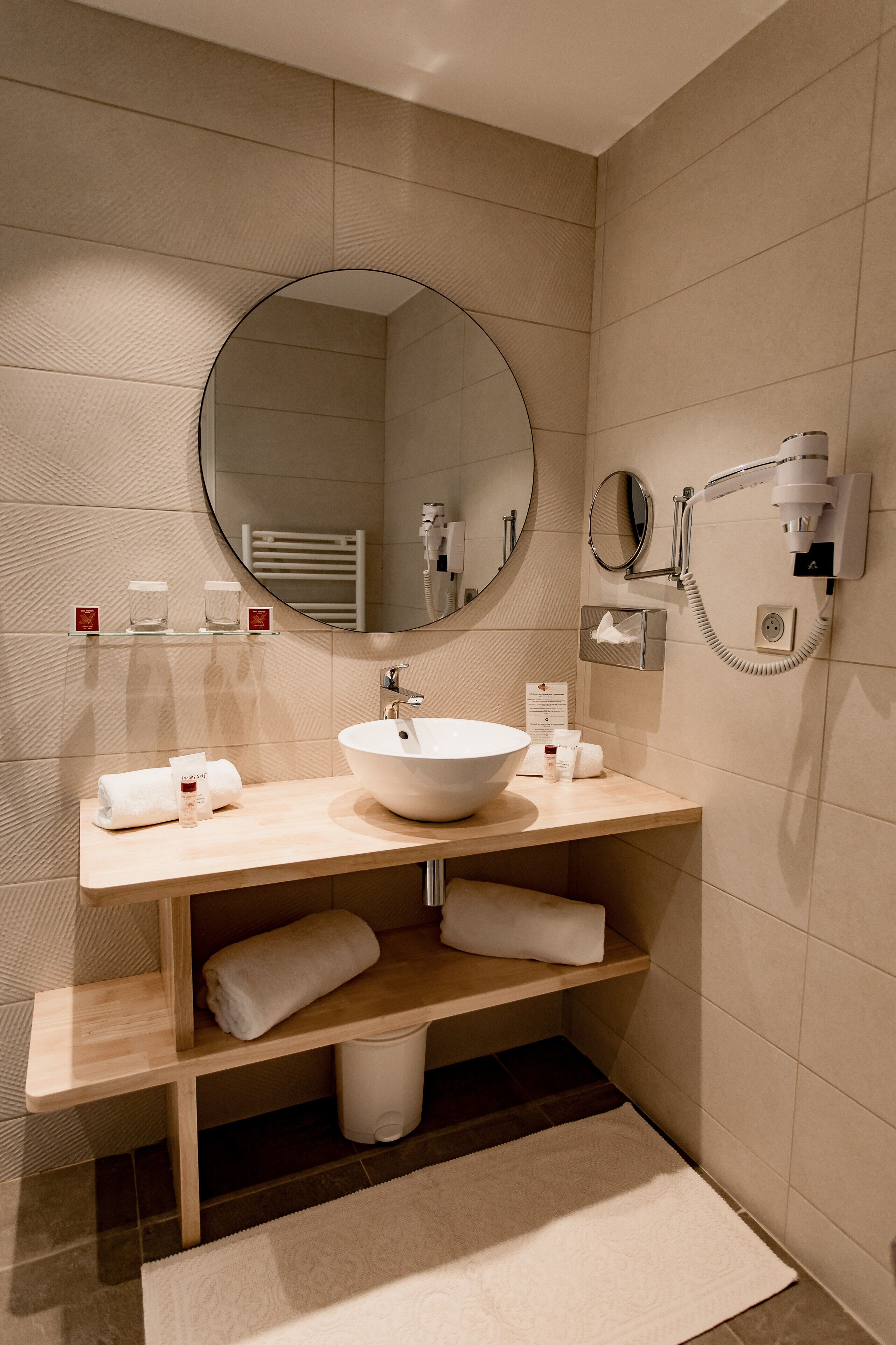 Een moderne badkamer met een grote ronde spiegel, een witte wastafel en een handdoekhouder.