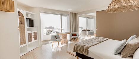 Una habitación de hotel moderna con una cama grande, una zona de comedor y un balcón con vistas.