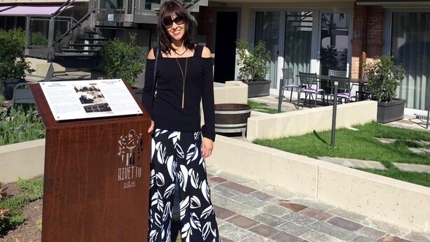 A woman standing in front of a building with a glass staircase and outdoor seating area. - Rivetto Suites (Alba)