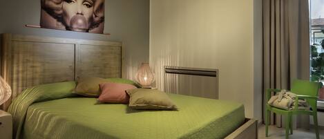 A bedroom with a green bed, a wooden headboard, a poster on the wall, a bedside lamp, and a chair with a cushion.