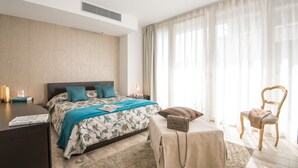 A modern hotel room with a large bed, a bedside table, a chair, and a view of the outdoors through sheer curtains. - Rivetto Suites (Alba)