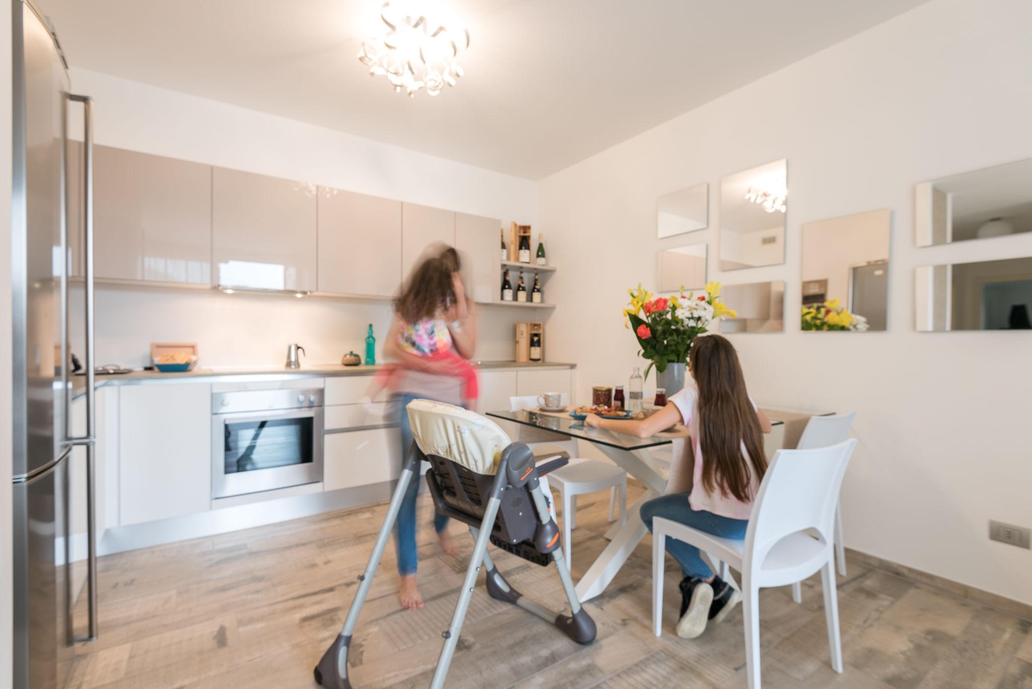 A modern kitchen with stainless steel appliances, a dining area with a table and chairs, and a large mirror on the wall.