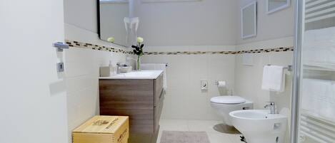 A modern bathroom with a wooden vanity, a bidet, a toilet, and a large mirror.