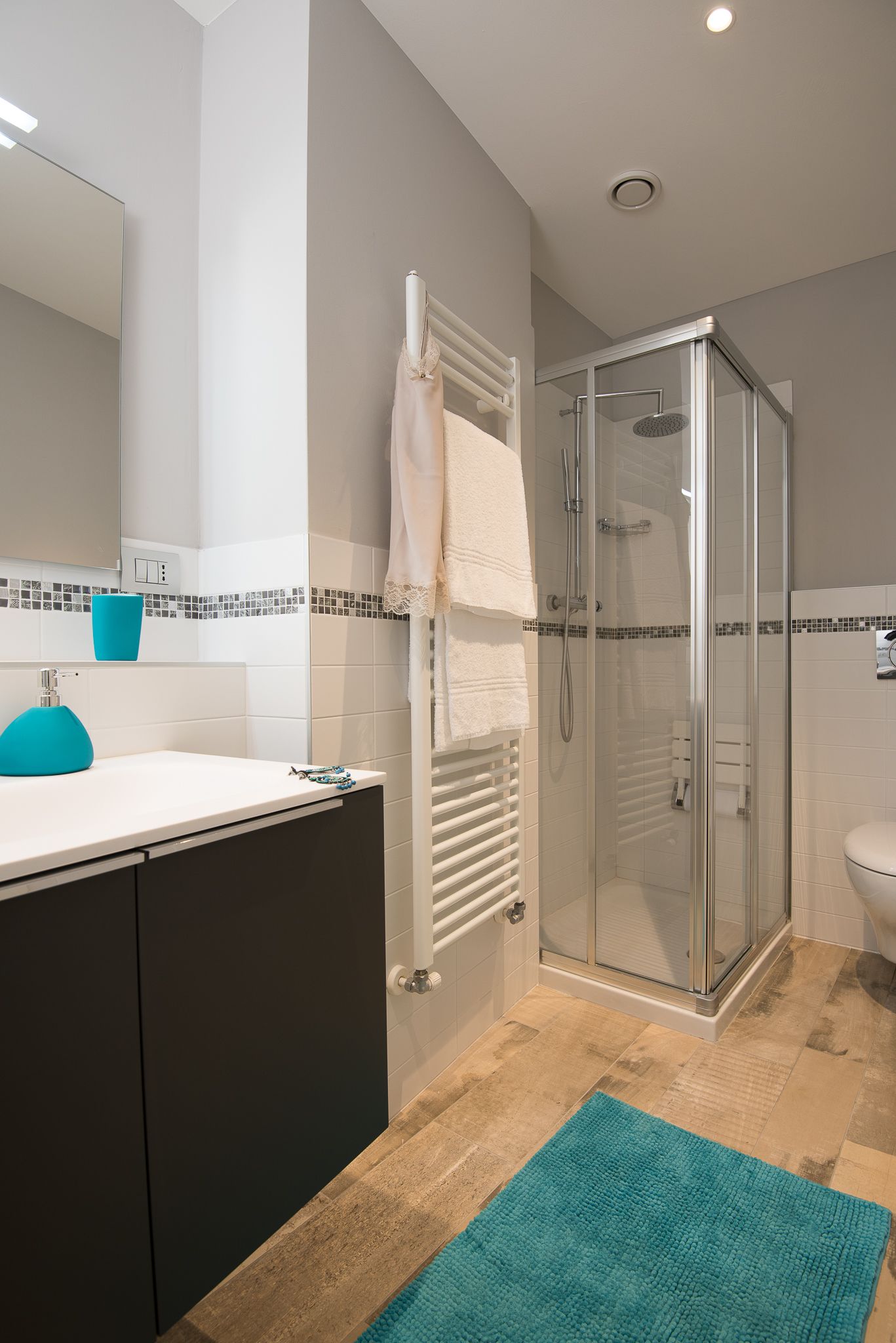 Ein modernes Badezimmer mit einer gläsernen Duschkabine, einem weißen Waschbecken mit blauem Akzent und einer gefliesten Rückwand.