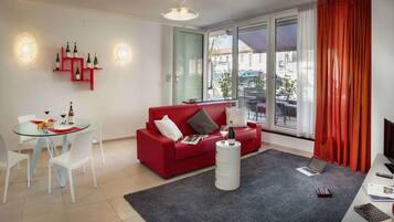 Ein modernes Wohnzimmer mit einem roten Sofa, einem Glastisch und einem großen Fenster mit Vorhängen.