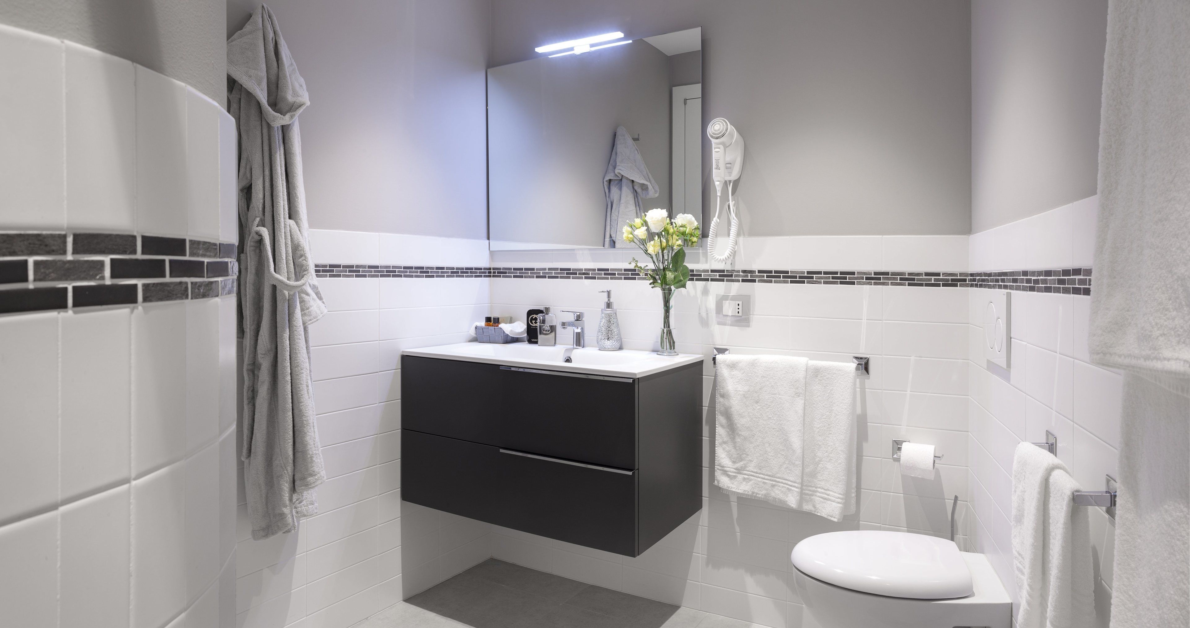 A modern bathroom with a white sink, dark cabinet, and a white toilet.
