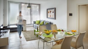 A modern living room with a glass dining table, a sofa with green cushions, and a framed artwork on the wall. - Rivetto Suites (Alba)