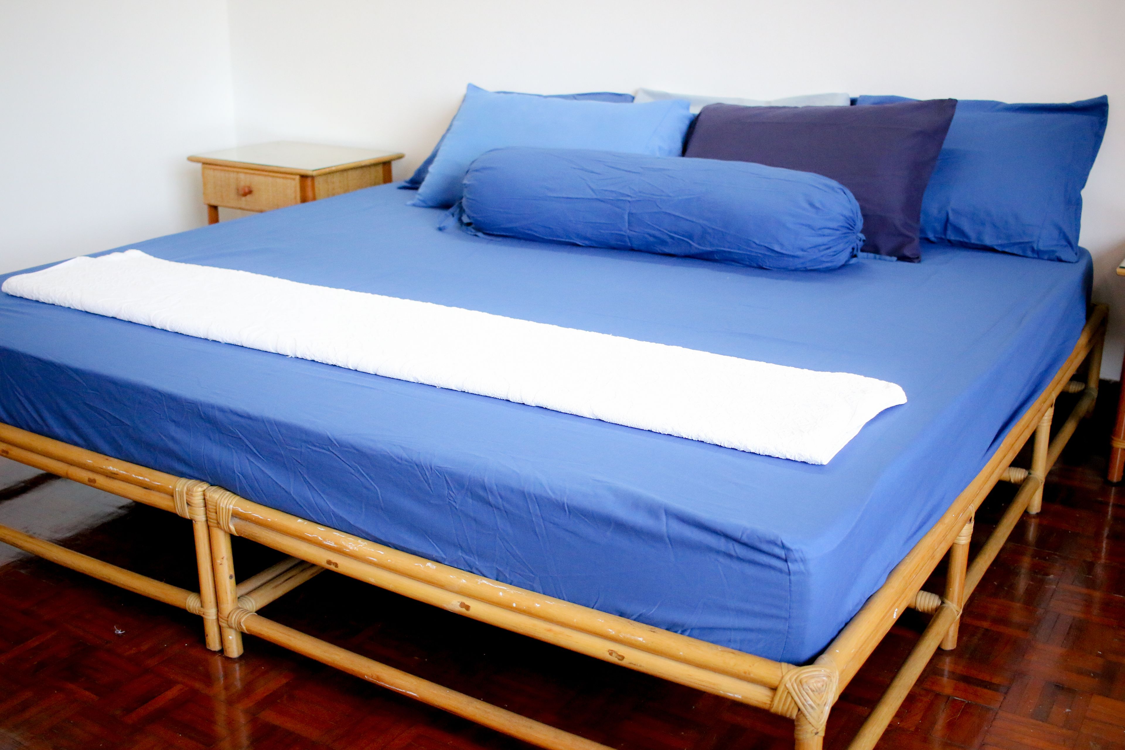 A bed with a blue mattress and pillows, a wooden frame, and a small wooden nightstand beside it.