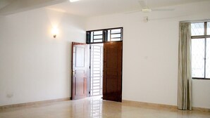 A spacious room with a tiled floor, a ceiling fan, a door with a window, and a wall-mounted light fixture.