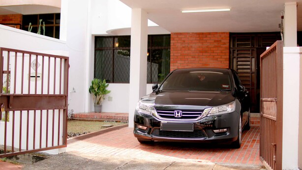 A Honda car parked in a covered driveway with a brick wall and a metal gate.