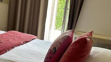 Een hotelkamer met een bed, kussens en een raam met gordijnen.