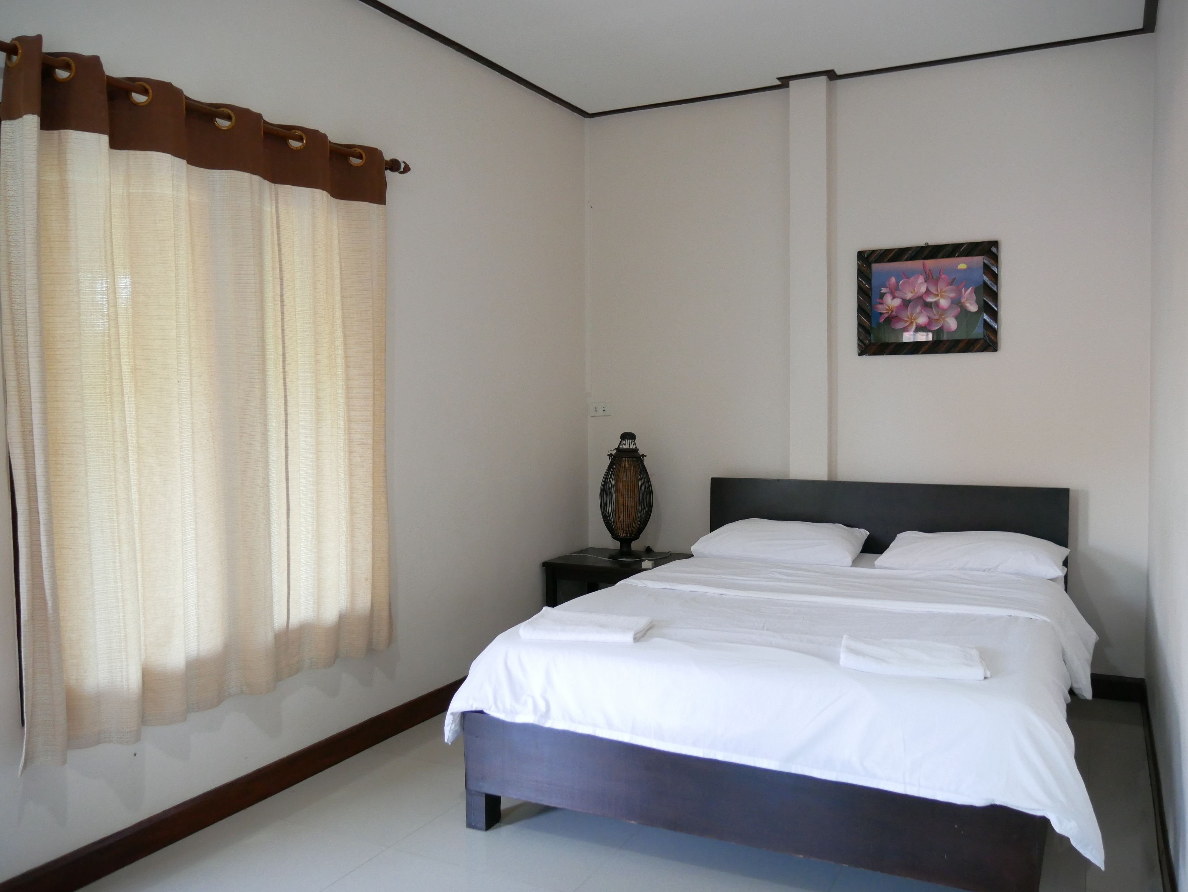 A bedroom with a bed, a nightstand, a lamp, a painting, and a window with curtains.