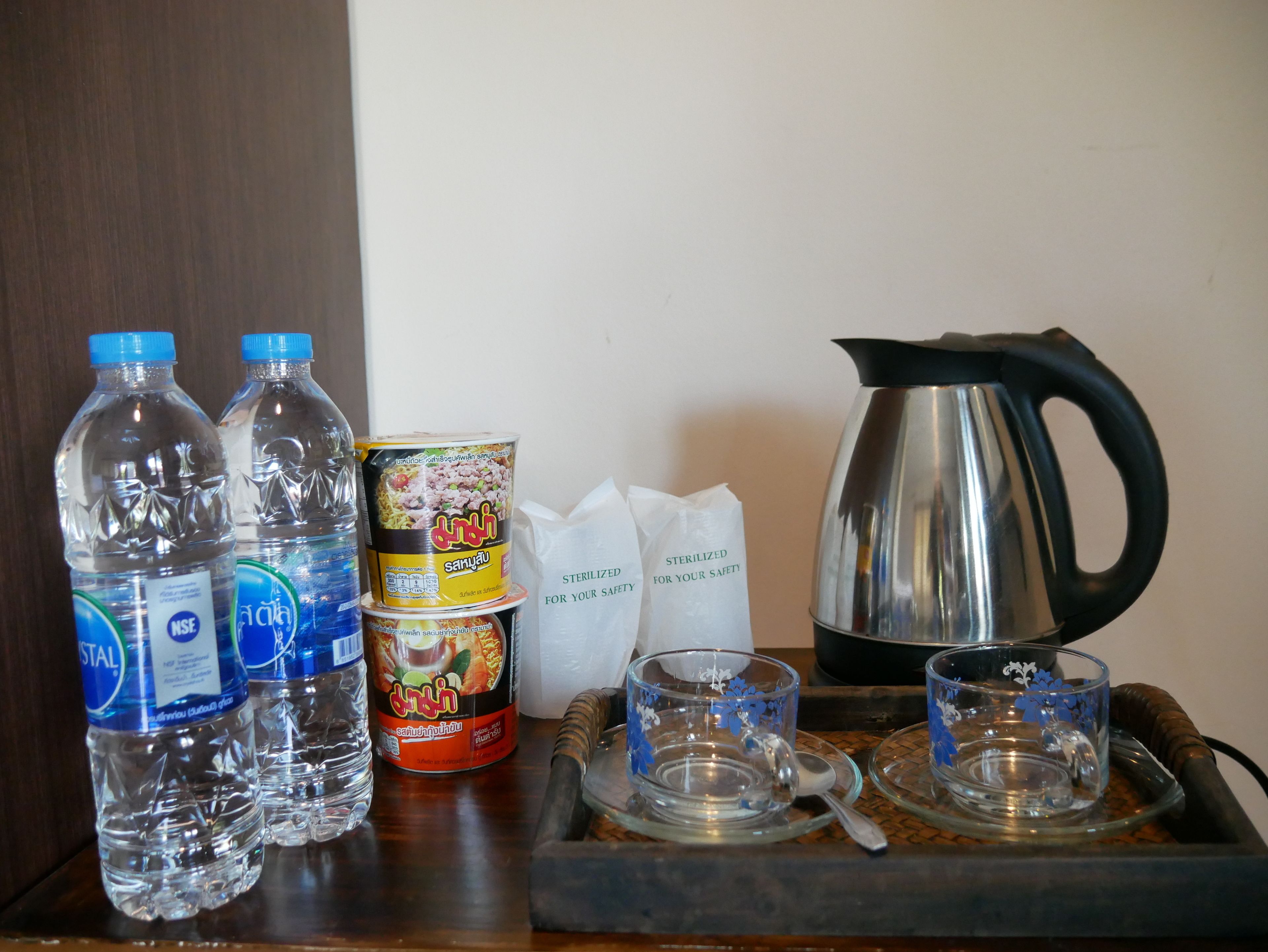 A tray with bottled water, canned food, a kettle, and glassware.