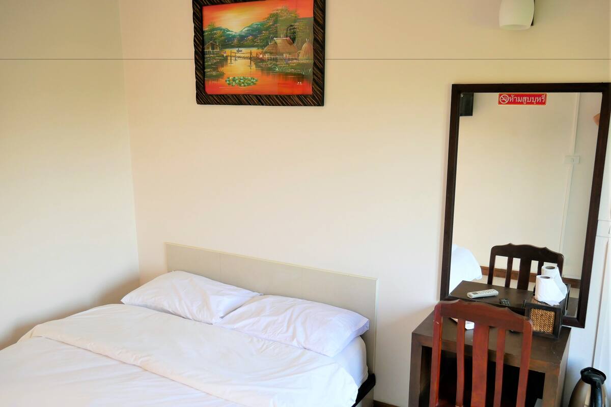 Una habitación de hotel con cama, una silla, una mesa con lámpara, un cuadro y un espejo.