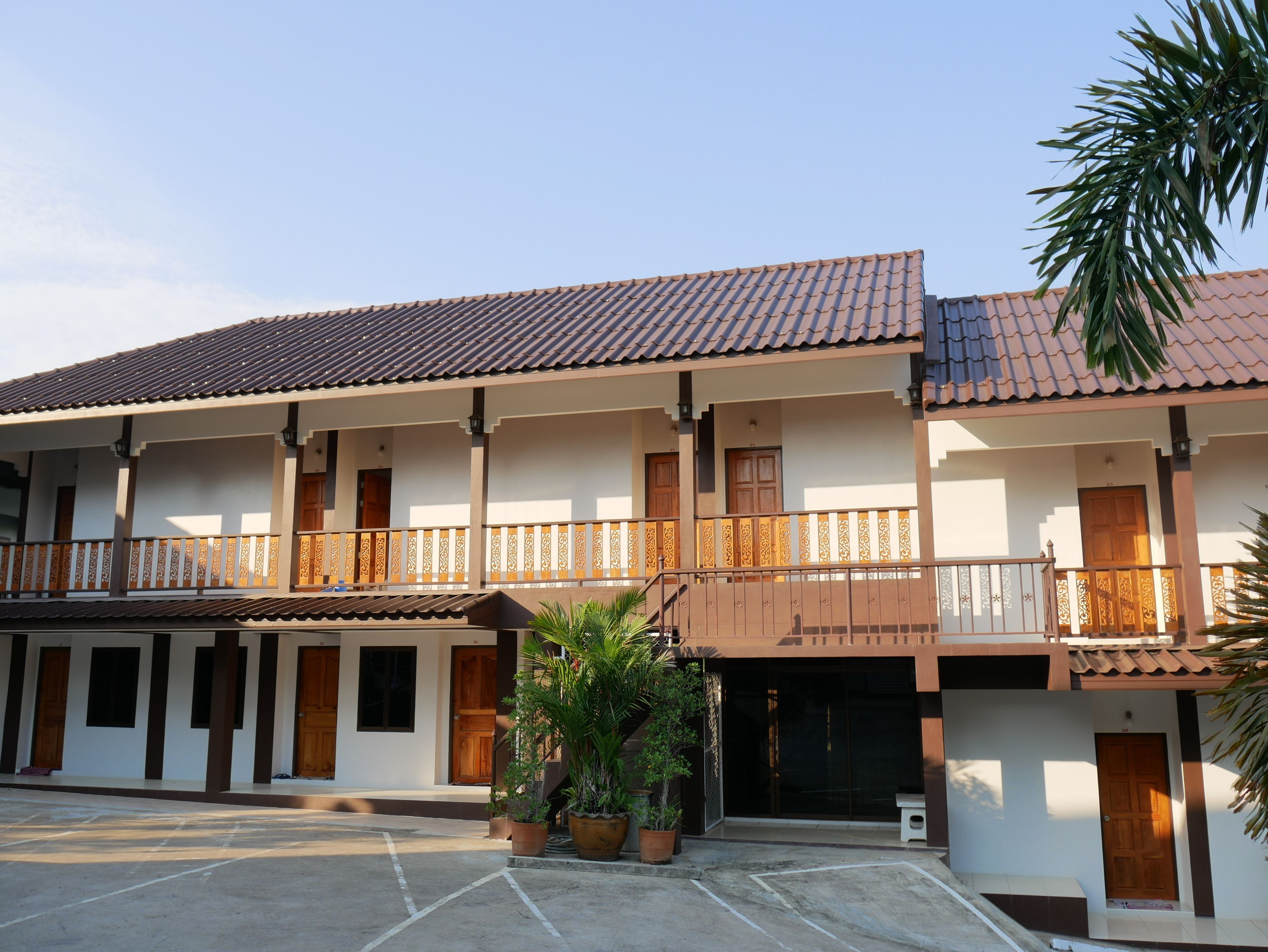 A two-story building with a tiled roof, multiple balconies with wooden railings, and potted plants in the courtyard.
