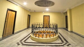 Un atrio circular con barandilla de metal decorativa, suelo de mármol y puertas de madera.