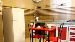 A compact kitchen with a red table and chairs, a white refrigerator, and a sink with a faucet. - Soleil d'Agadir Centre (Agadir)