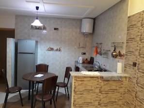 A kitchen with a dining table, chairs, a refrigerator, a sink, and a wooden accent wall.