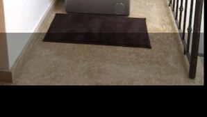 A compact, silver front-loading washing machine in a corner of a room with a small, dark mat on the floor. - Soleil d'Agadir Centre (Agadir)