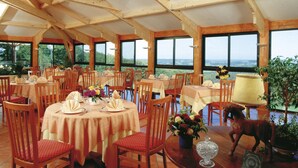 Un restaurant avec des tables et des chaises en bois, de grandes fenêtres et une vue sur l’extérieur.