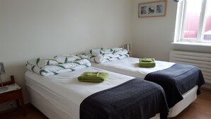 Une chambre avec un grand lit et deux lits simples, chacun étant équipé d’une serviette verte et d’une couverture foncée.