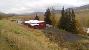 Un bâtiment rouge avec un toit blanc, entouré de pelouse et d’arbres, avec des montagnes en arrière-plan.