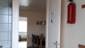Une pièce avec une porte blanche, un extincteur rouge fixé au mur et un mur recouvert de carreaux, avec un lavabo.