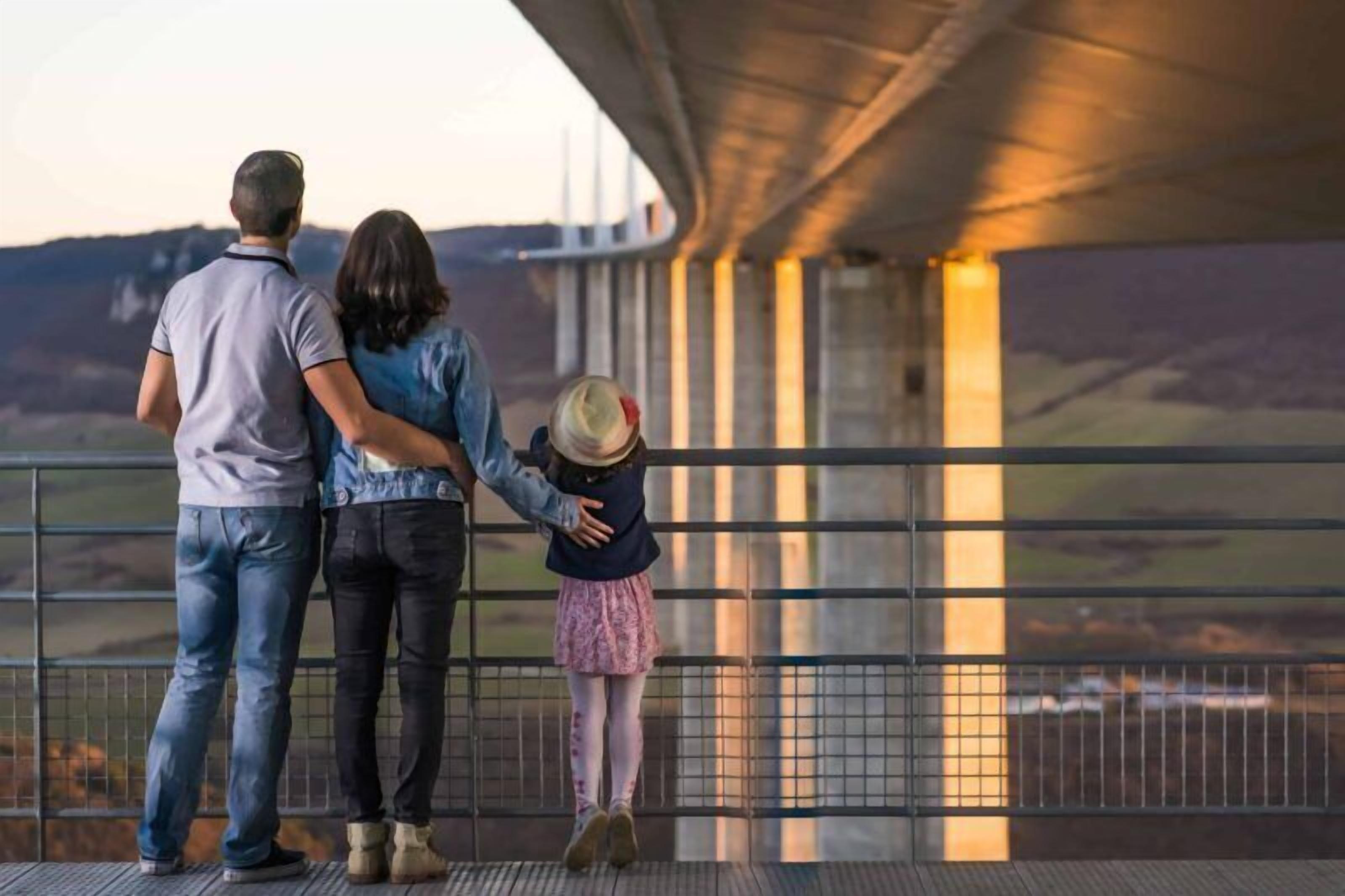 A family standing on a bridge railing overlooking a valley.