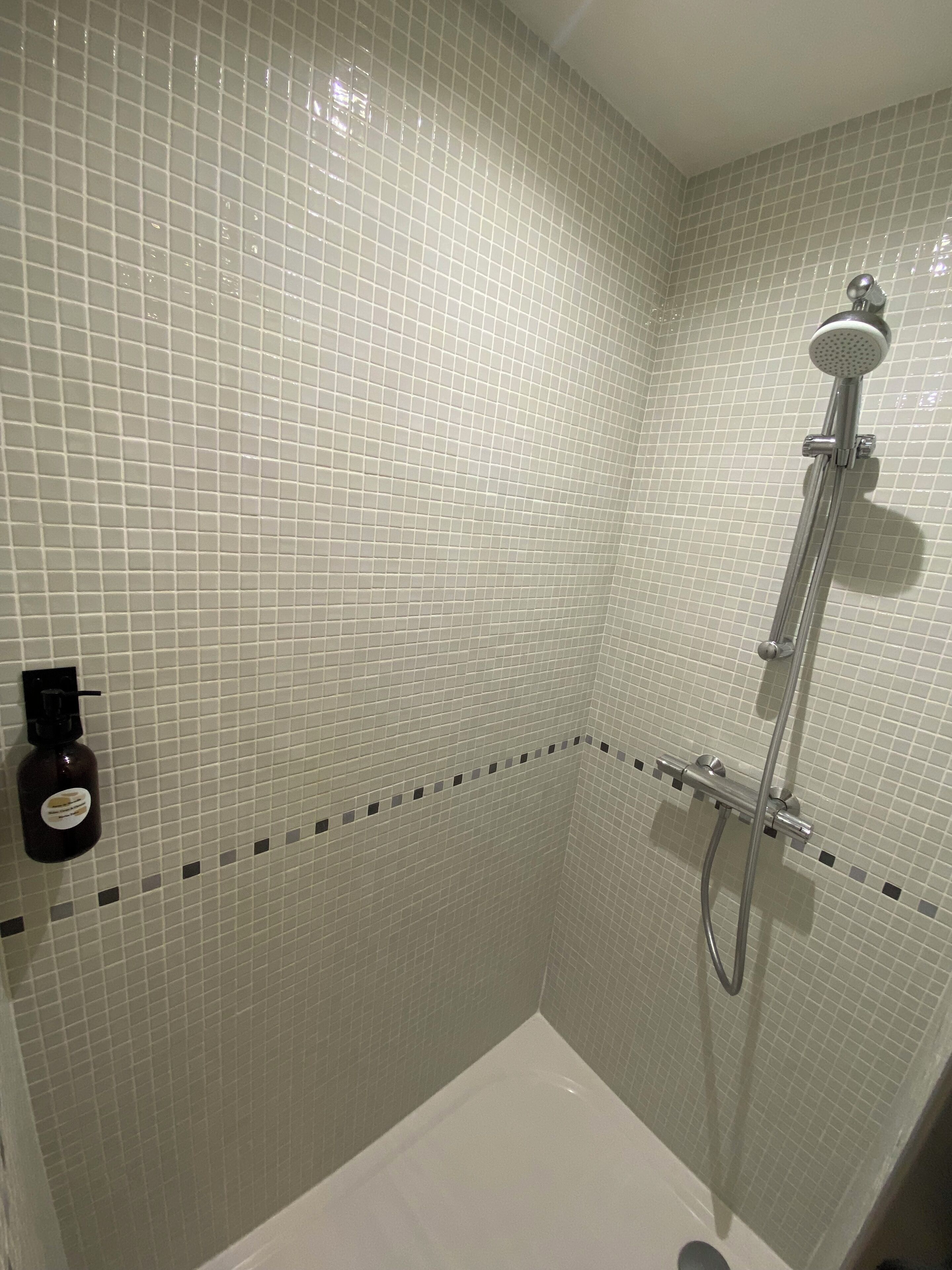 A bathroom with a white bathtub, a shower with a handheld showerhead, and a bottle of shampoo on the wall.