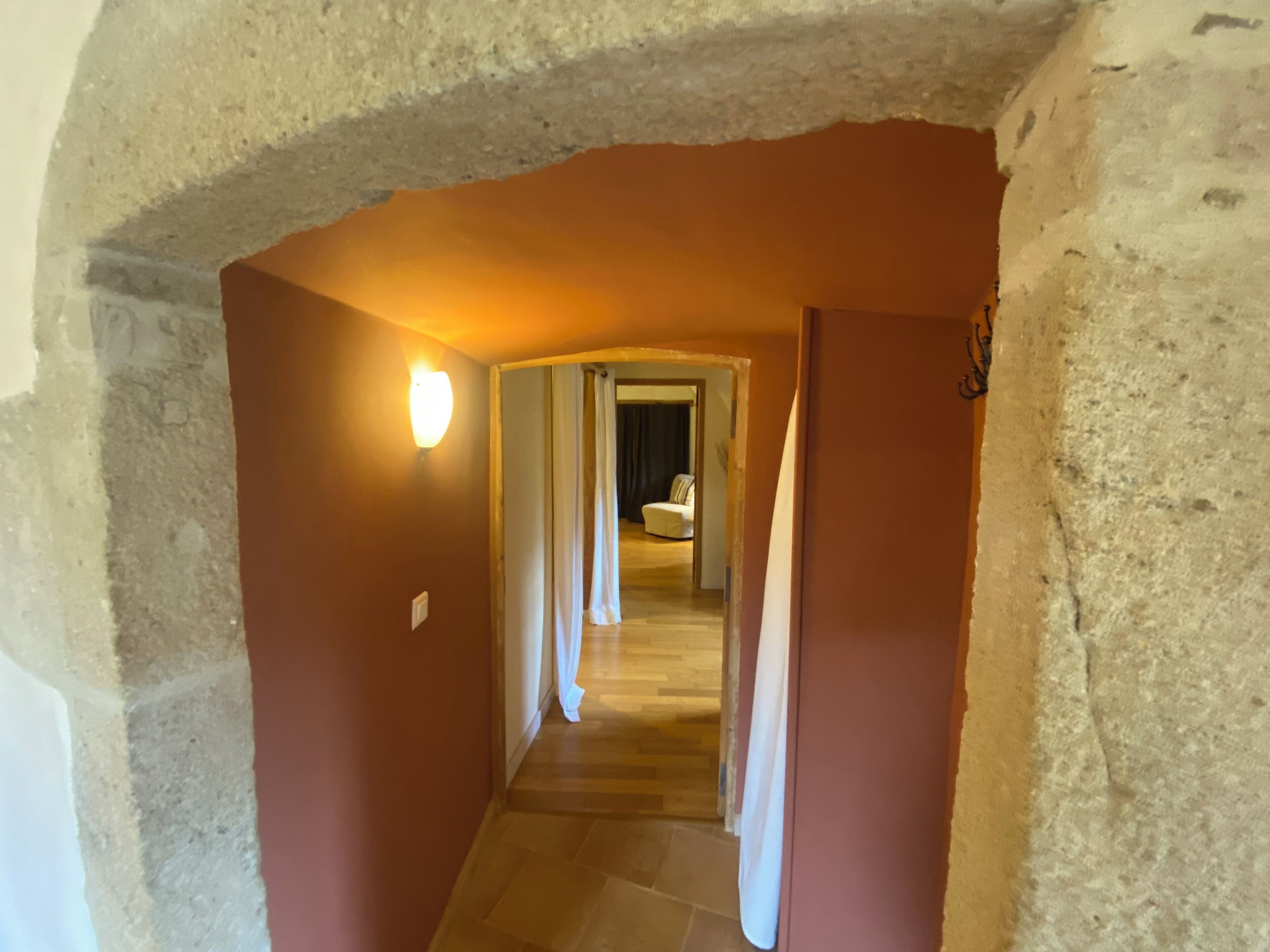 Un estrecho pasillo con un arco de piedra que conduce a una habitación con una cama y un ventanal.