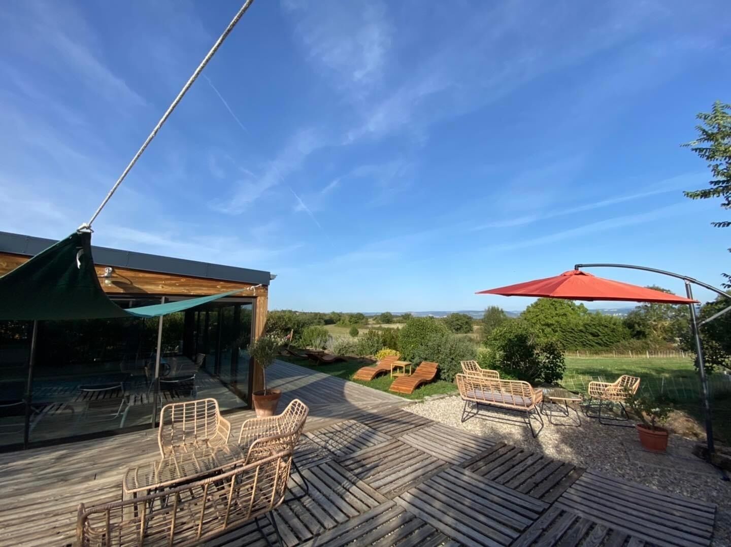 Una terraza de madera con mobiliario exterior, un espacio de estar cubierto y vistas al campo.
