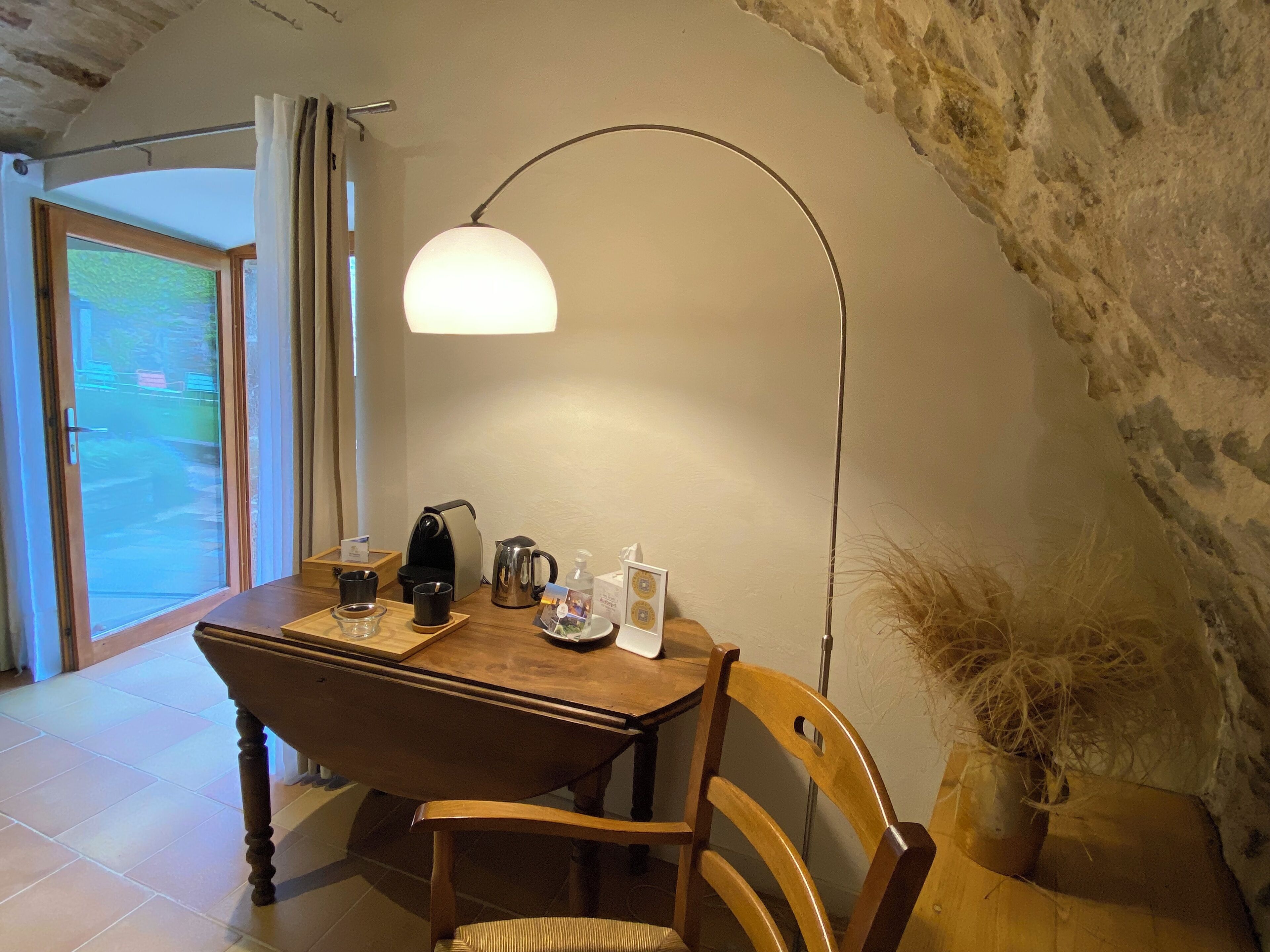 A cozy dining area with a wooden table, chairs, a coffee maker, cups, and a decorative vase.