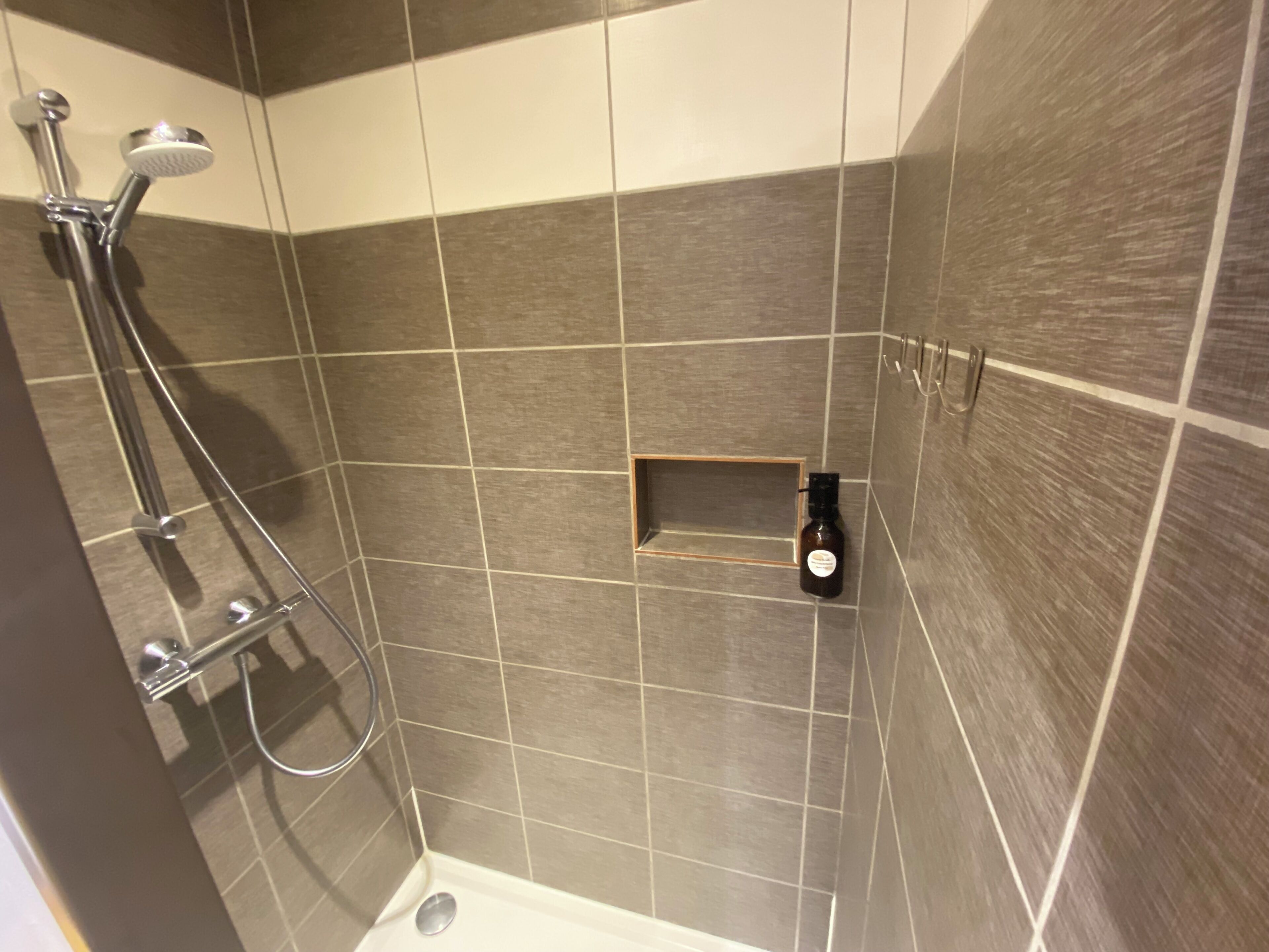 Douchegedeelte met douchekop, wandmengkraan en klein plankje met een fles.