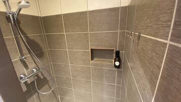 Douchegedeelte met douchekop, wandmengkraan en klein plankje met een fles.