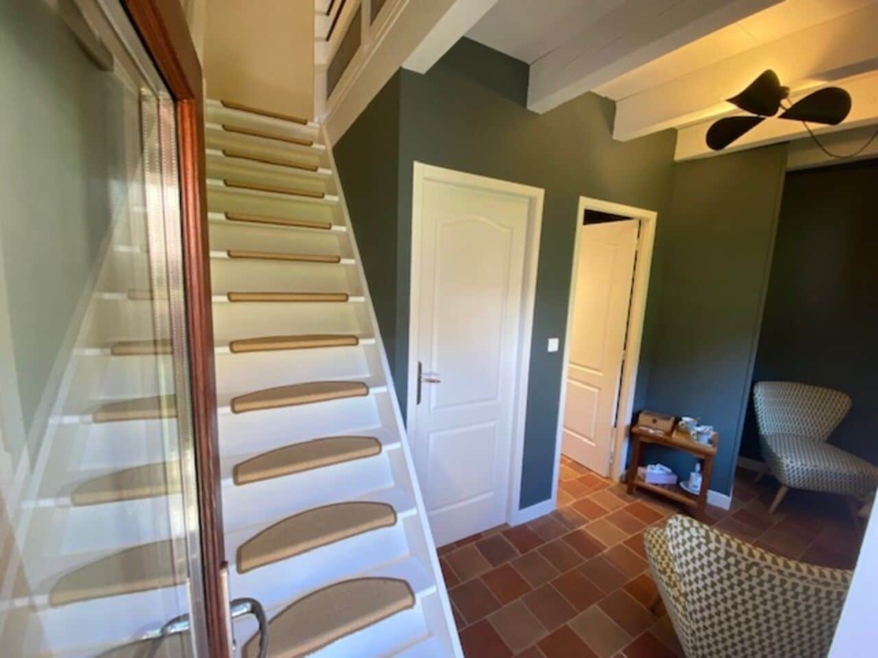 Un escalier avec une rampe, une porte fermée et une chaise dans une pièce dont le sol est recouvert de carreaux.