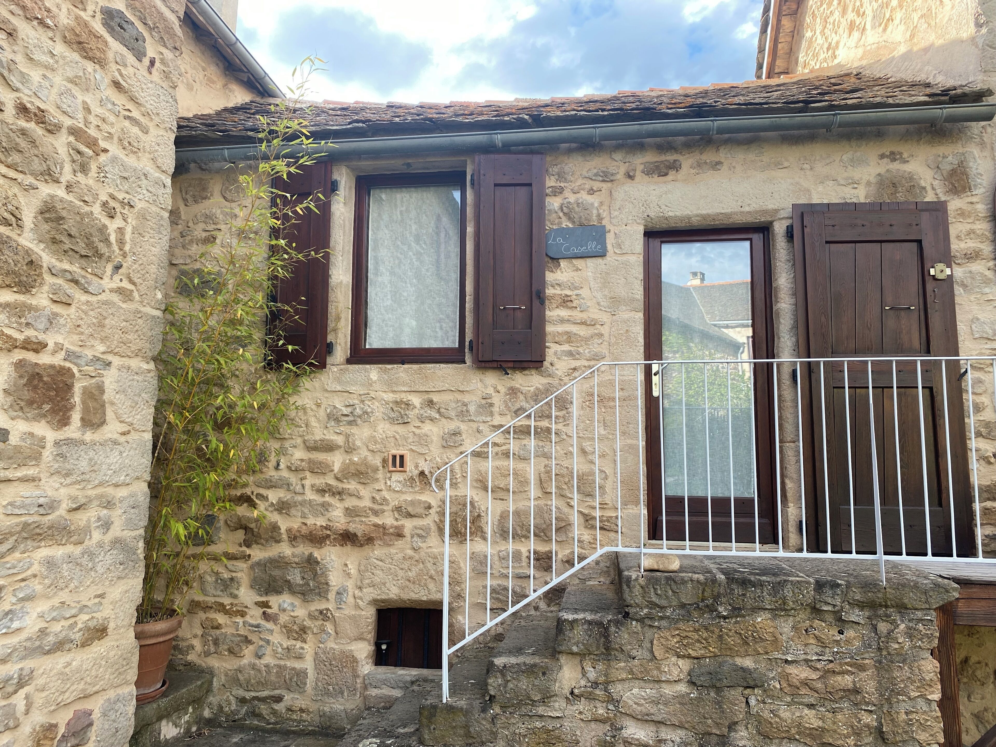 Un edificio de piedra con puerta de madera, una ventana con cortina y un pequeño balcón con barandilla de metal.
