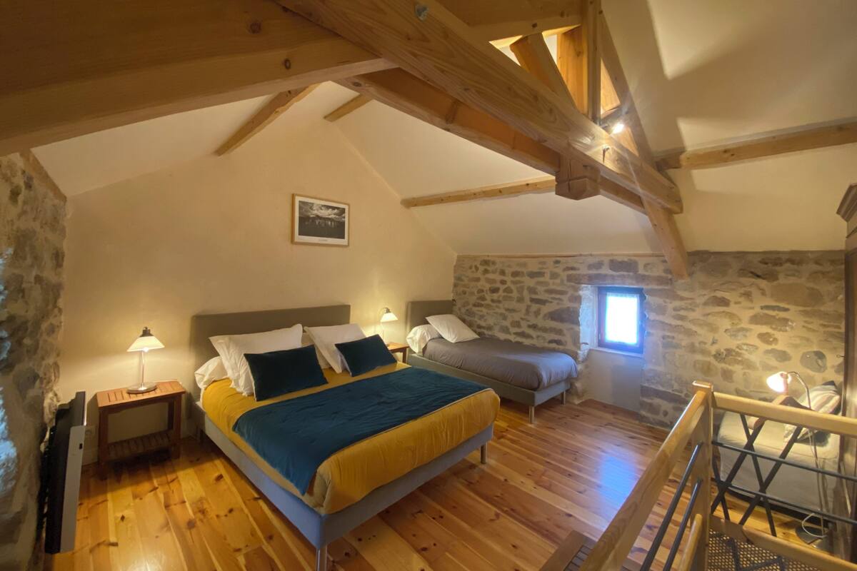 Um quarto de sótão acolhedor, com teto de madeira, parede de pedra e cama com colcha azul e amarela.