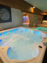 A hot tub with blue LED lights, a stone wall, and a wooden ceiling.