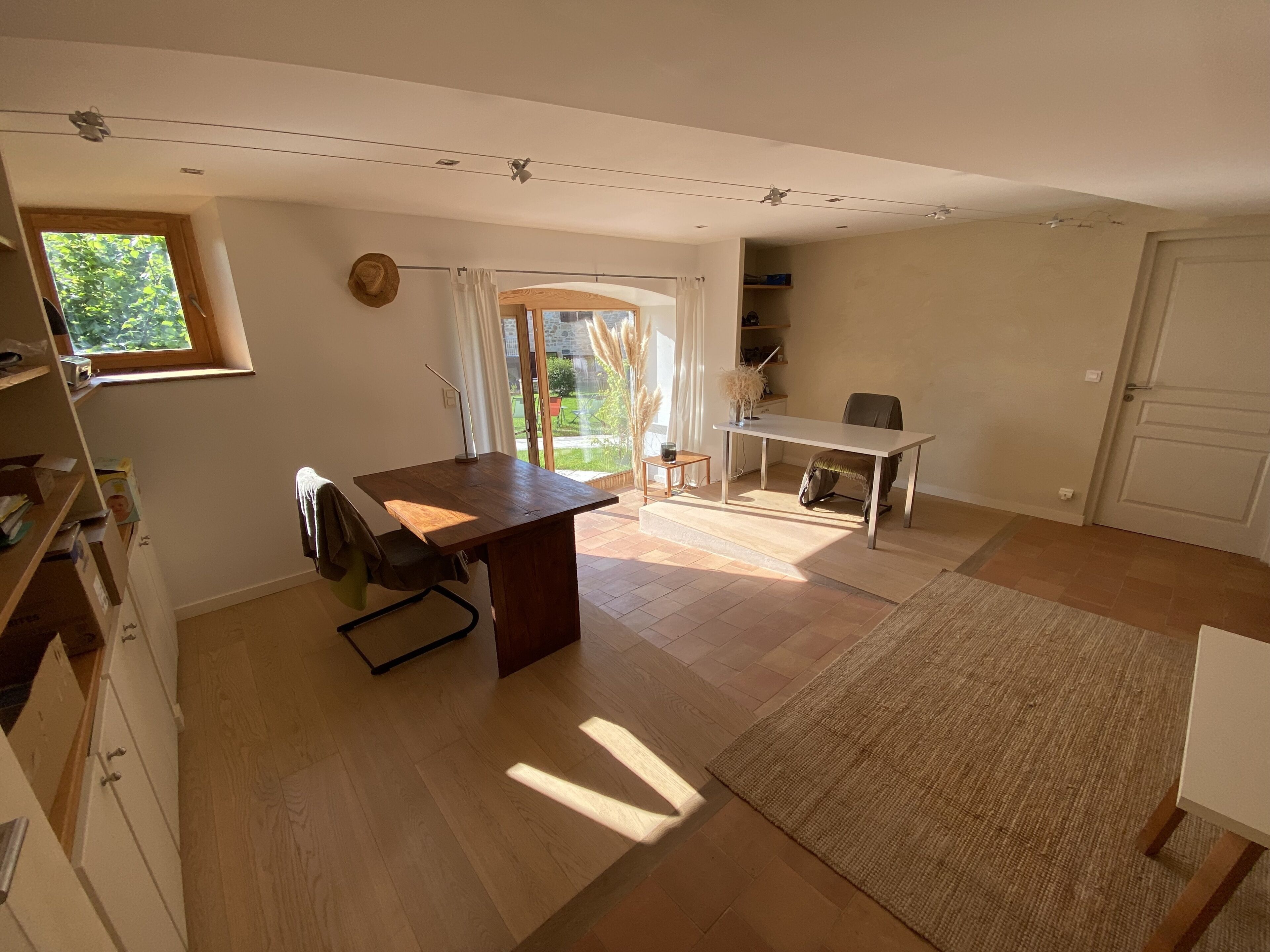 Ein geräumiges Zimmer mit einem Holztisch, einem Stuhl, einem kleinen Tisch und einem großen Fenster.
