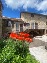 A stone building with a balcony, a wooden bridge, and red poppies in the foreground.