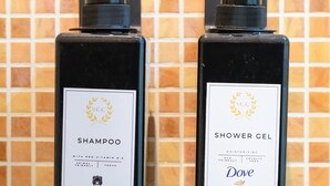 Zwei schwarze Flaschen mit Dove Shampoo und Duschgel vor einer gefliesten Wand.
