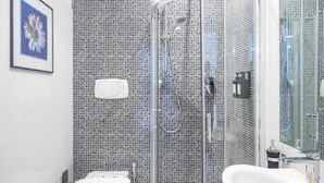 Ein modernes Badezimmer mit Duschkabine aus Glas, einem weißen Waschbecken und einem gerahmten Blumenbild an der Wand.