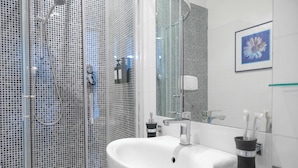 Ein modernes Badezimmer mit Duschkabine aus Glas, einem weißen Waschbecken und einem gerahmten Bild an der Wand.