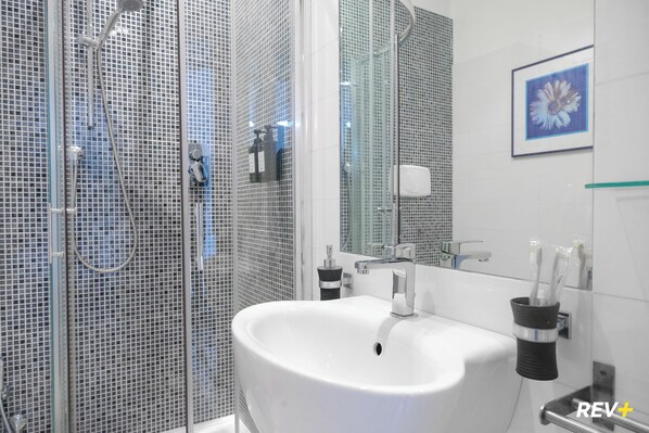 Un baño moderno con cabina de ducha de vidrio, un lavabo blanco y un cuadro enmarcado en la pared.