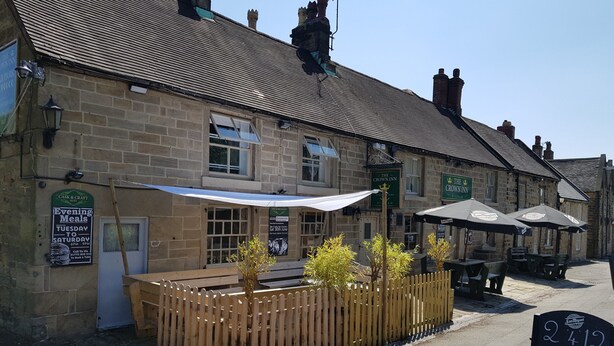 A traditional stone building with a sign for 'The Crown Inn' and an outdoor seating area with umbrellas. - The Crown Inn (Alfreton)