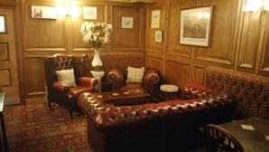 A room with a leather sofa, a matching armchair, a small table, and a decorative vase with flowers. - The Crown Inn (Alfreton)