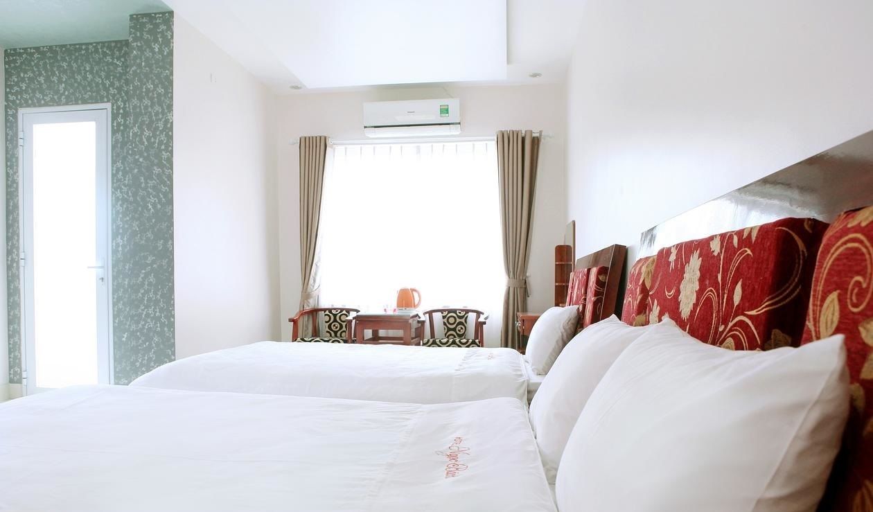 Habitación de hotel con dos camas, un escritorio con sillas, una ventana con cortinas y un equipo de aire acondicionado.