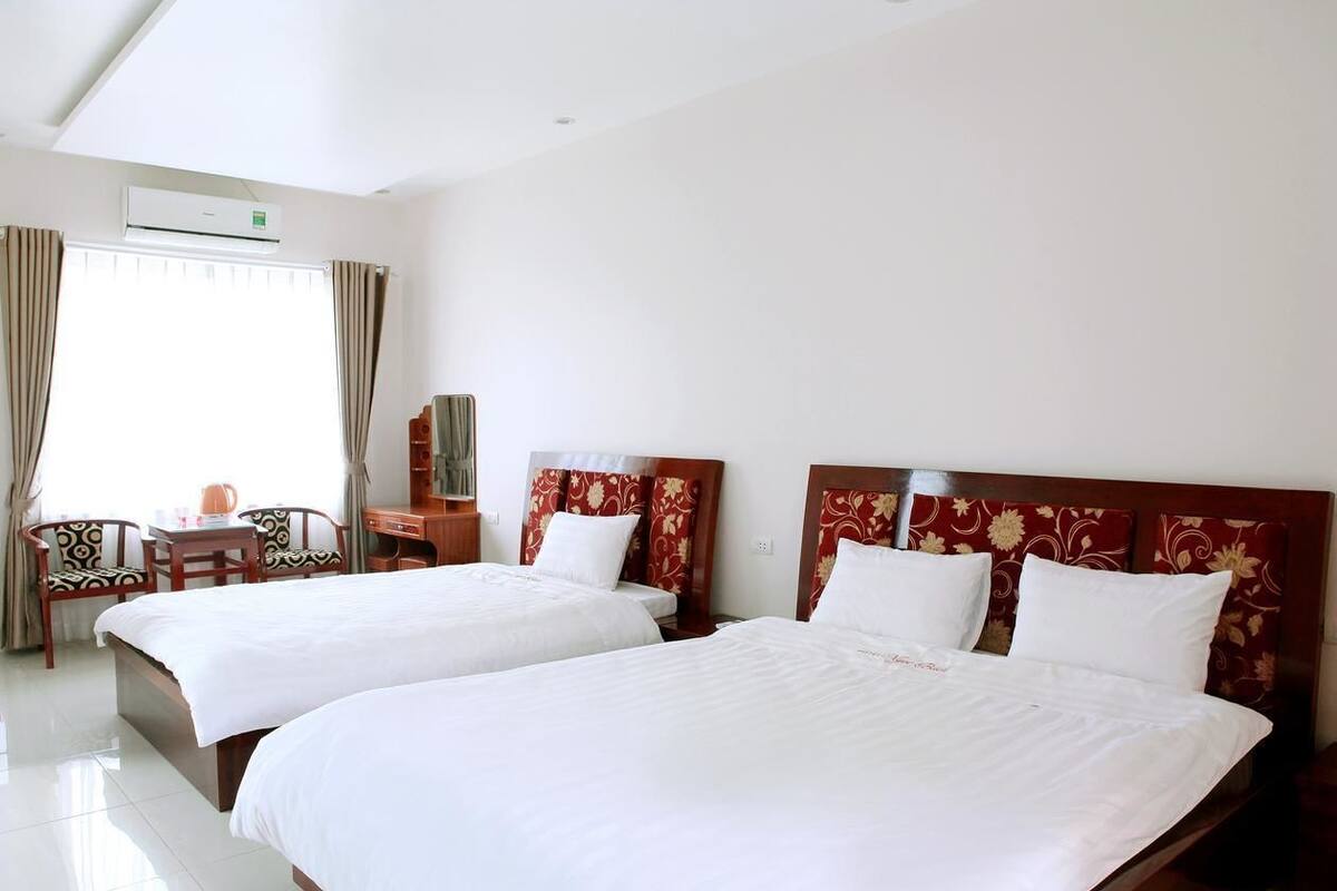 Quarto de hotel com duas camas, uma mesa, cadeiras e aparelho de ar condicionado.