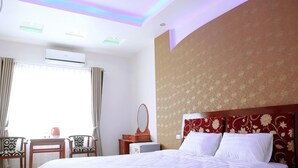 Una habitación de hotel con una cama, un escritorio con silla, un tocador con espejo y un equipo de aire acondicionado.