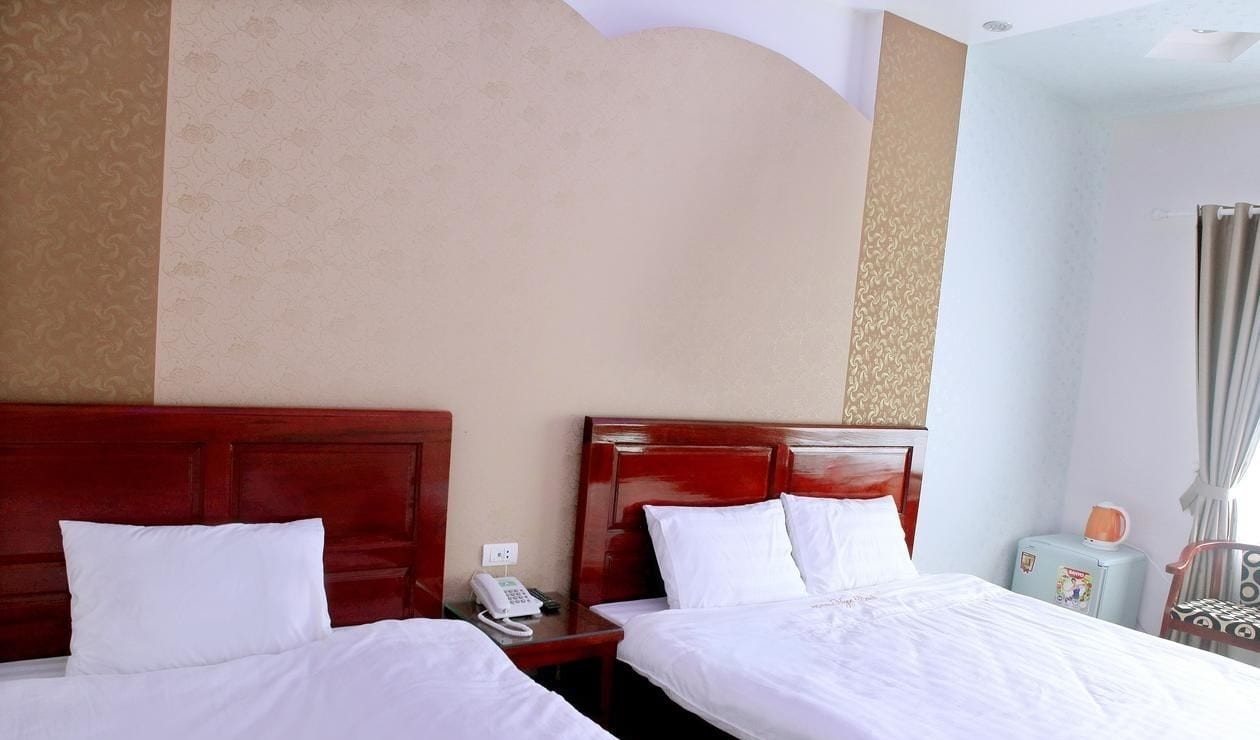 Habitación de hotel con dos camas, cabeceros de madera, una mesita de noche con un teléfono y una mesita de noche con una lámpara.